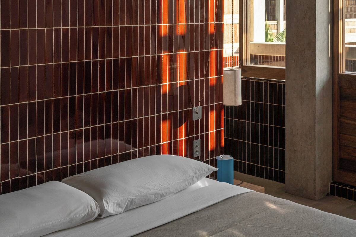 A hotel room with a bed, a wooden wall with vertical slats, a window, and a concrete pillar.