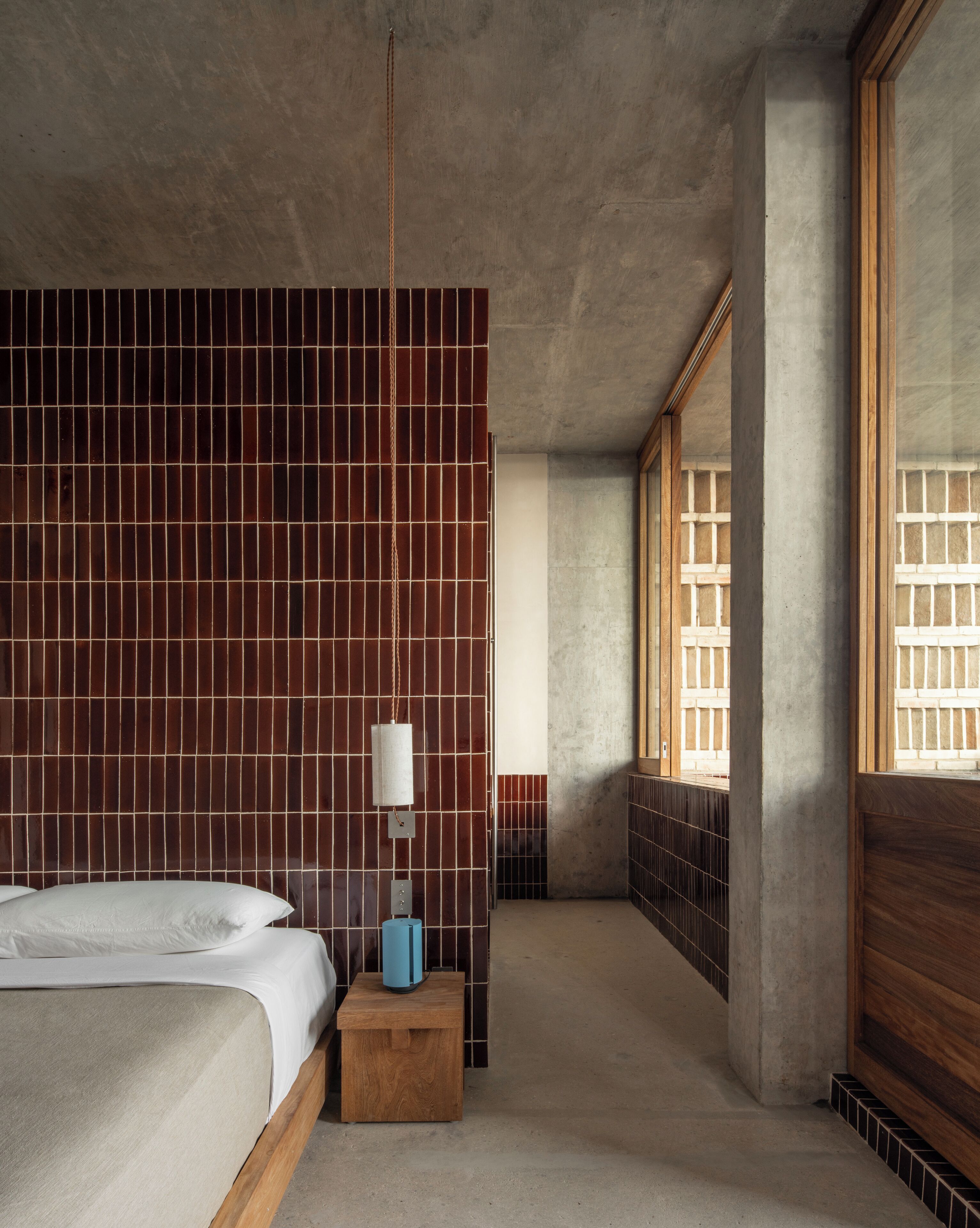 Una habitación de hotel moderna con una cama grande, una mesita de noche, una lámpara y vistas al exterior a través de un amplio ventanal.