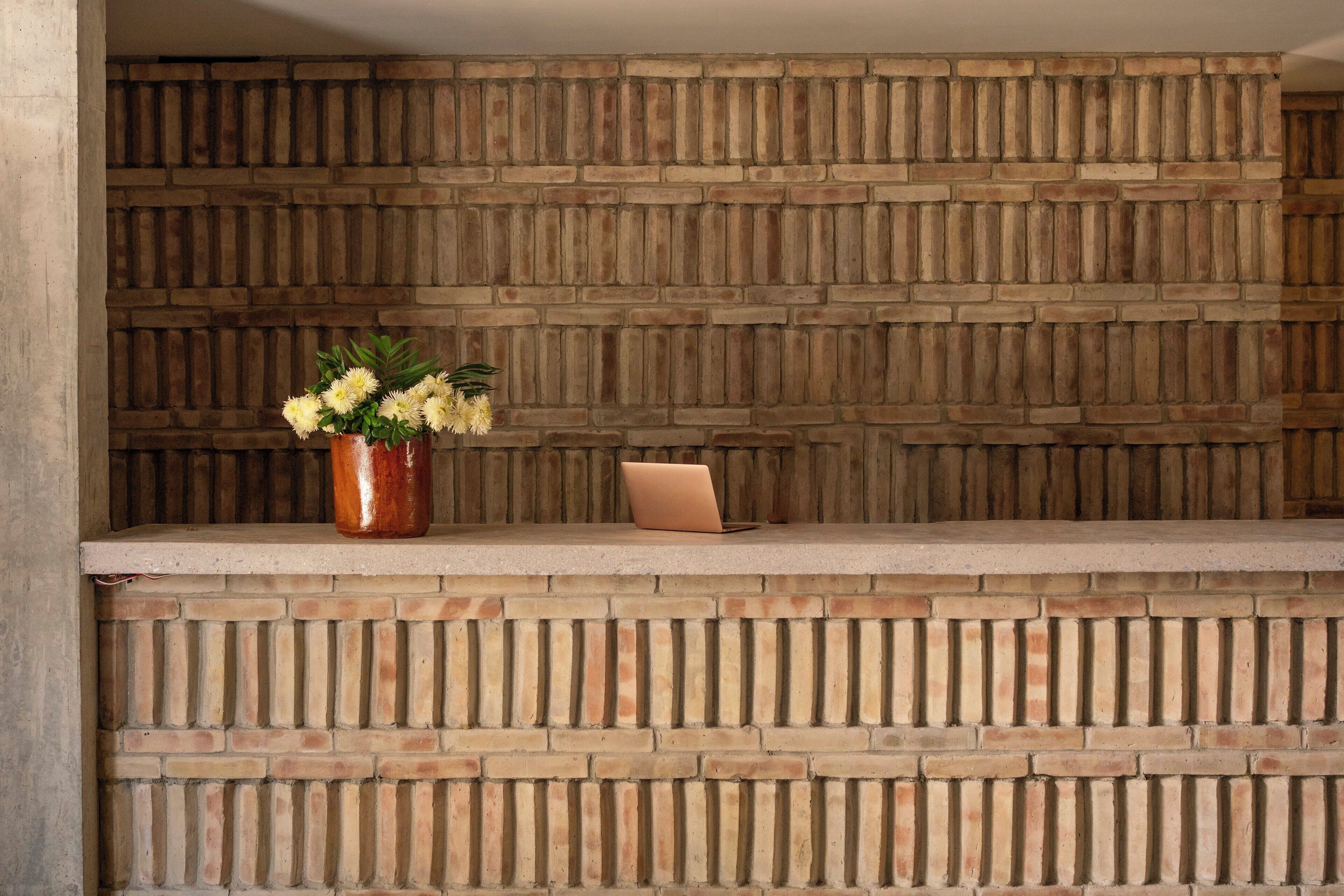 A reception desk with a brick wall backdrop, a vase with flowers, and a laptop.
