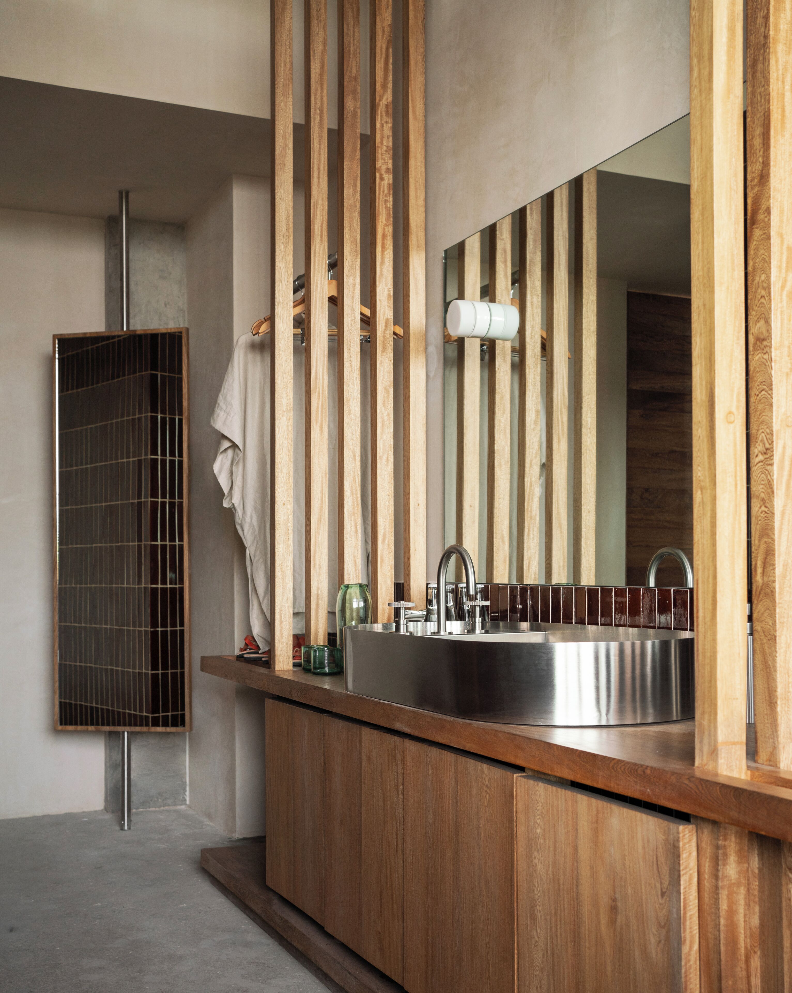 Un baño moderno con tocador de madera, lavamanos de acero inoxidable y un espejo grande.