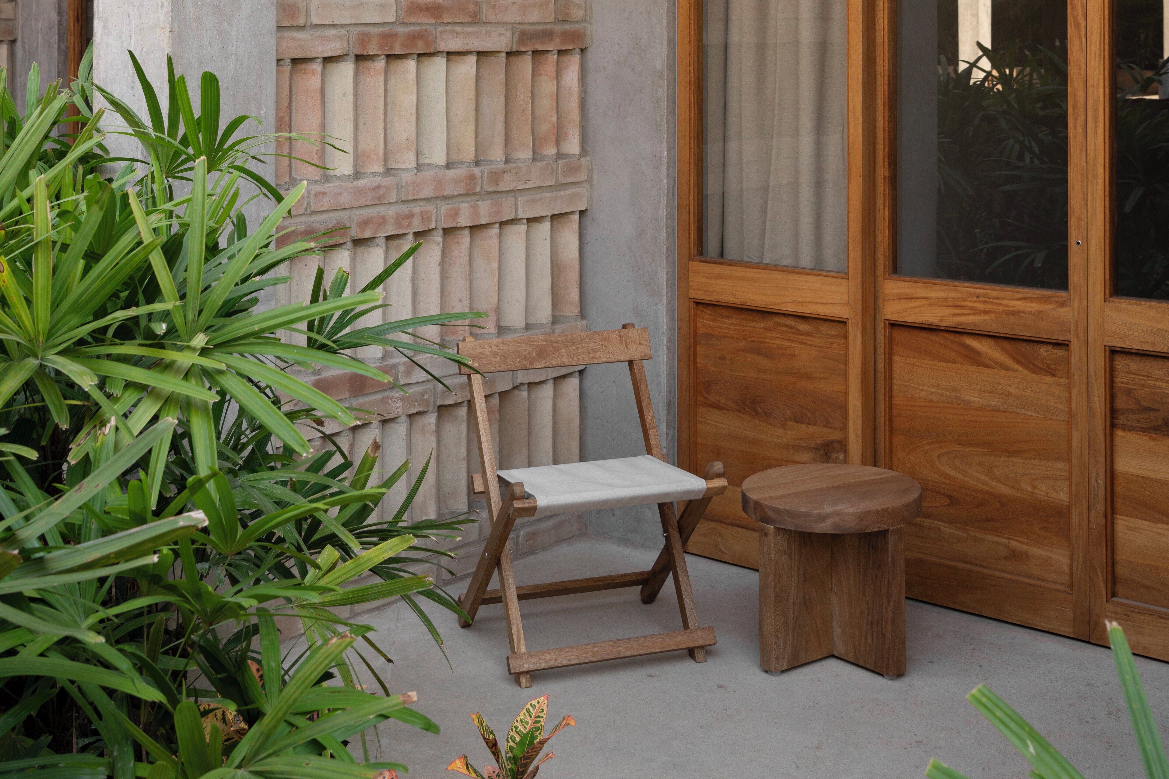 A wooden bench and stool outside a building with a brick wall and large windows.