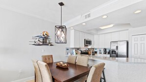 Una cocina moderna con armarios blancos, un refrigerador de acero inoxidable y un comedor con mesa y sillas de madera.