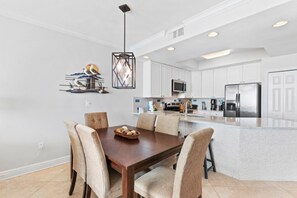 A modern kitchen with white cabinets, a stainless steel refrigerator, and a dining area with a wooden table and chairs.