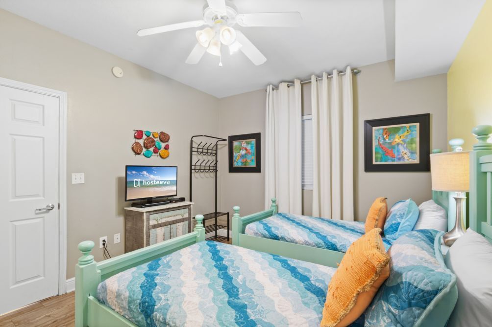 A bedroom with two beds, a ceiling fan, a television, and artwork on the walls.