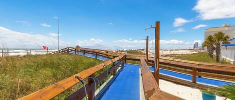 Una pasarela de madera que conduce a una playa, bajo un cielo despejado.
