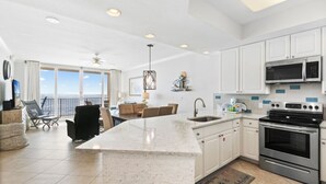 Una cocina moderna con armarios blancos, una isla grande, electrodomésticos de acero inoxidable y vistas al exterior.