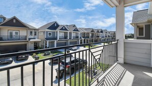 A row of townhouses with attached garages, a balcony with a railing, and a clear blue sky. - Cozy & Stylish Family Friendly in Gated Community (Sugar Land)