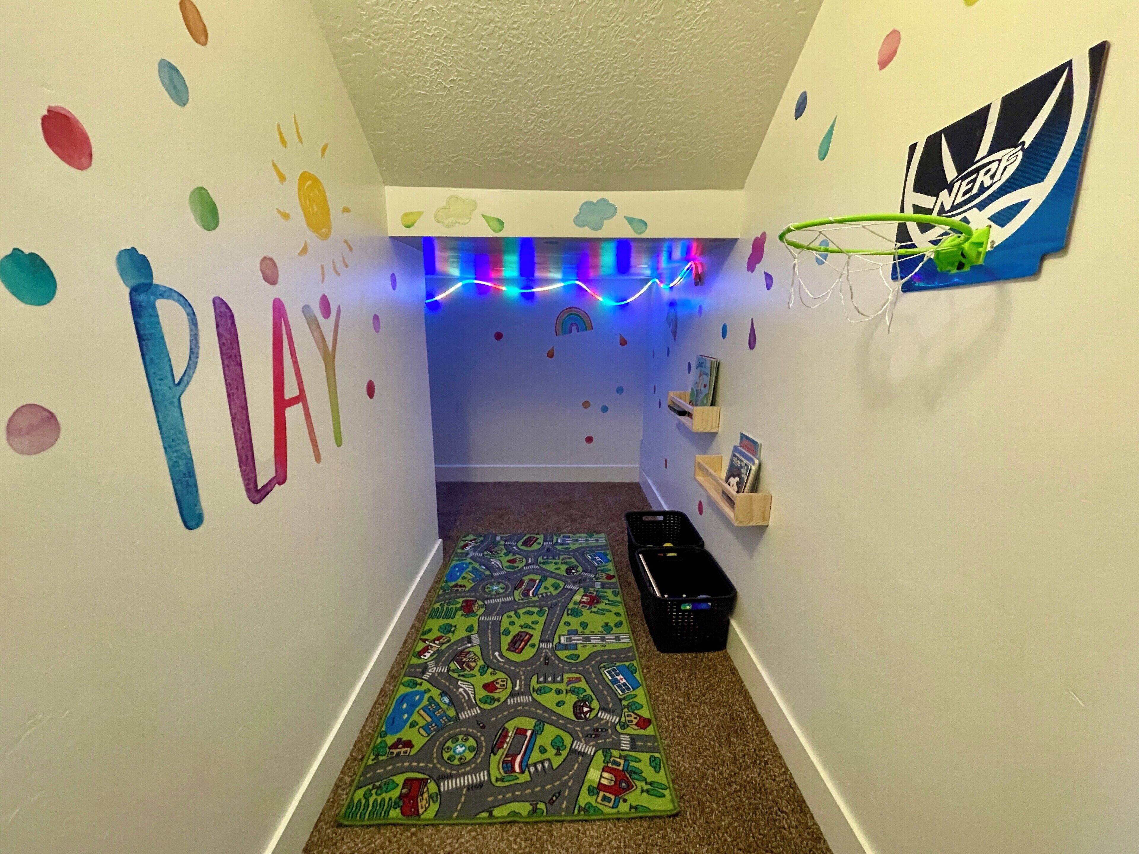 A child's playroom with a colorful play mat, wall decorations, and a shelf with books.