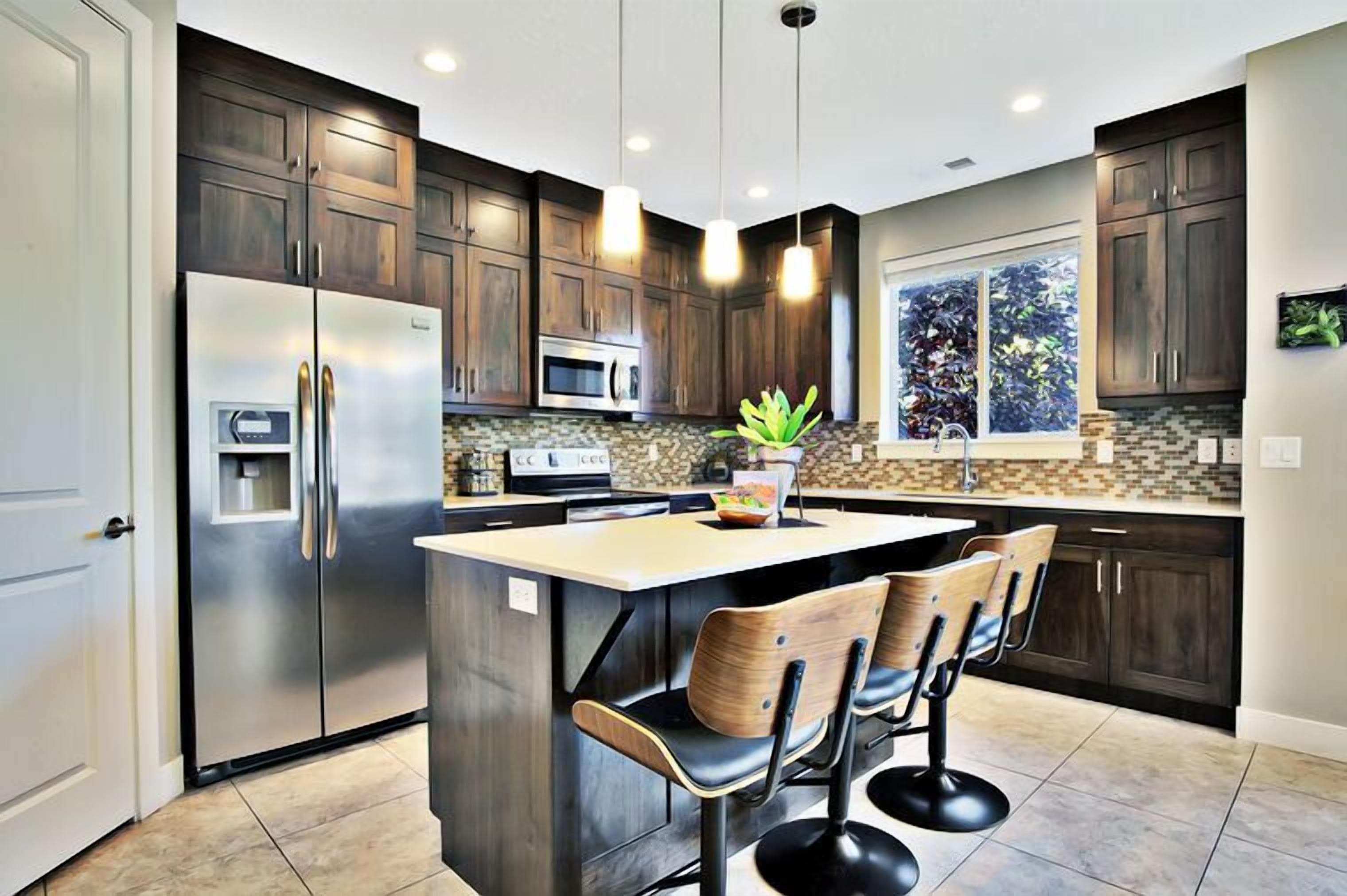 A modern kitchen with dark wood cabinets, stainless steel appliances, a central island with bar stools, and pendant lighting.
