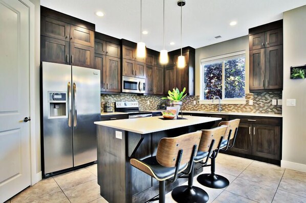 A modern kitchen with dark wood cabinets, stainless steel appliances, a central island with bar stools, and pendant lighting.