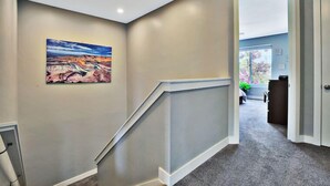 A hallway with a painting of a canyon landscape, a staircase, and a door leading to another room.