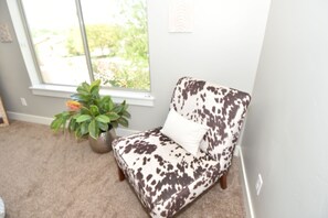 Ein Zimmer mit Fenster, ein Sessel mit gepunktetem Kissen und einer Topfpflanze.