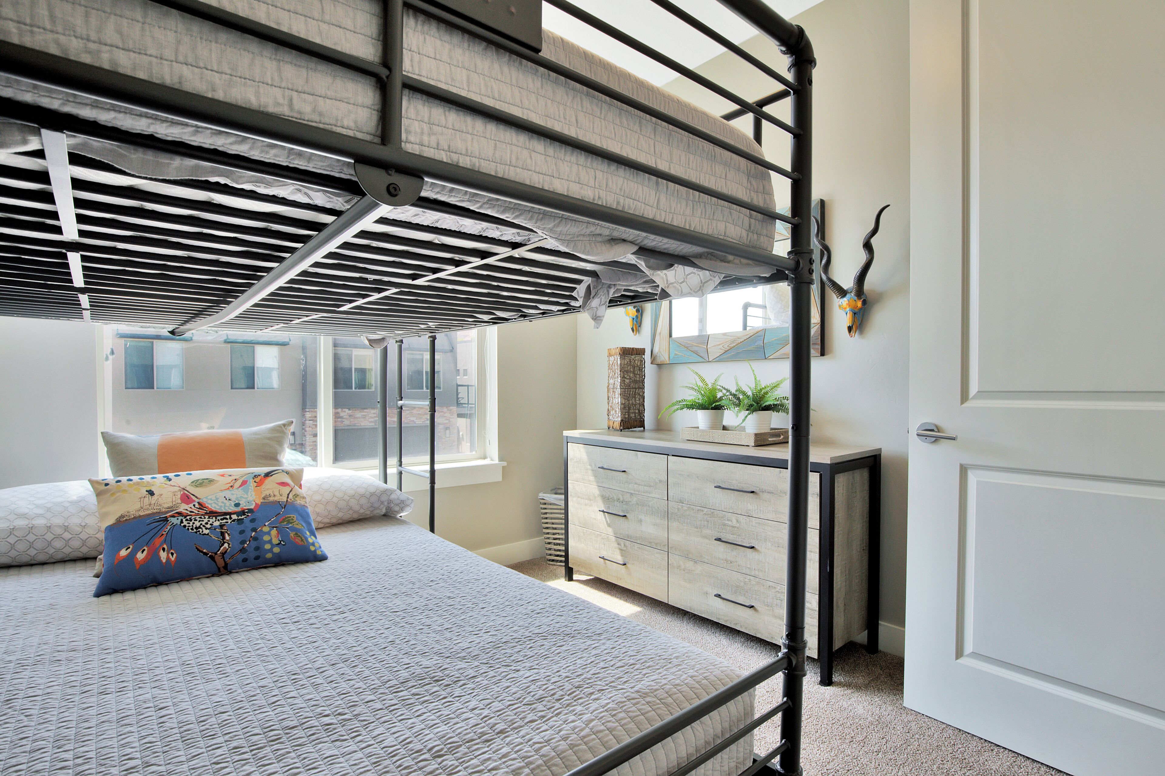A bunk bed with a metal frame, a bedside table with a plant, and a dresser with drawers.
