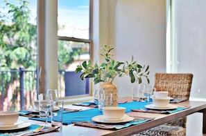 A dining table set with plates, bowls, and glasses, a vase with green plants, and a wicker chair.