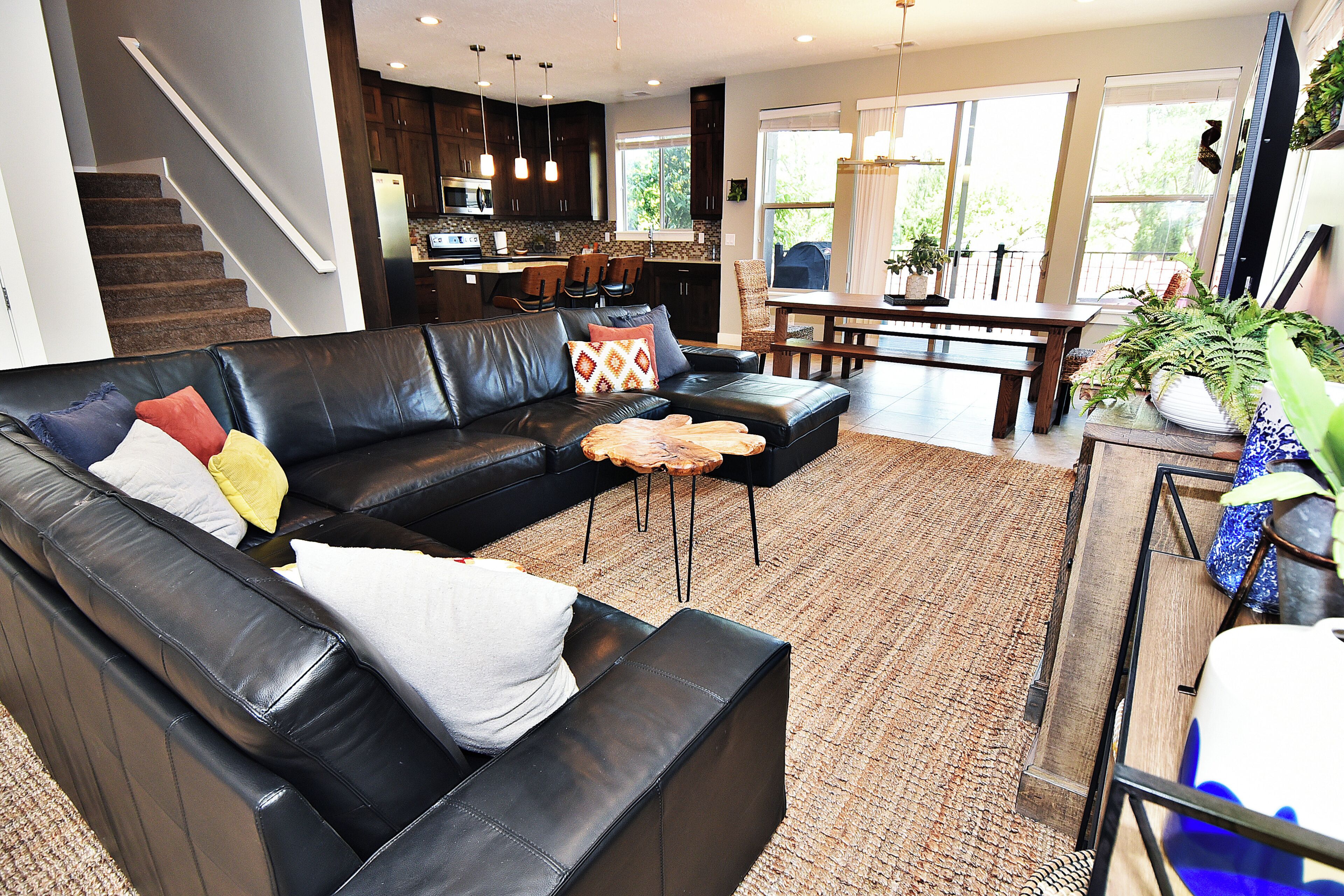 A modern living room with a black leather sofa, a dining table, and a kitchen in the background.