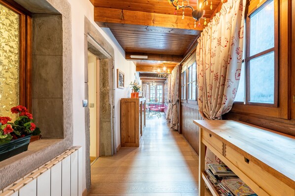 A corridor with wooden beams, a wooden bench, and a window with floral curtains.