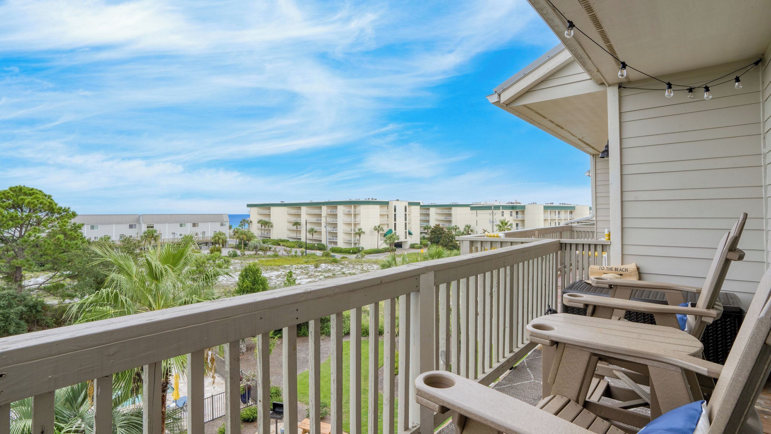 A balcony with outdoor furniture, a view of a beach, and a hotel building in the background.
