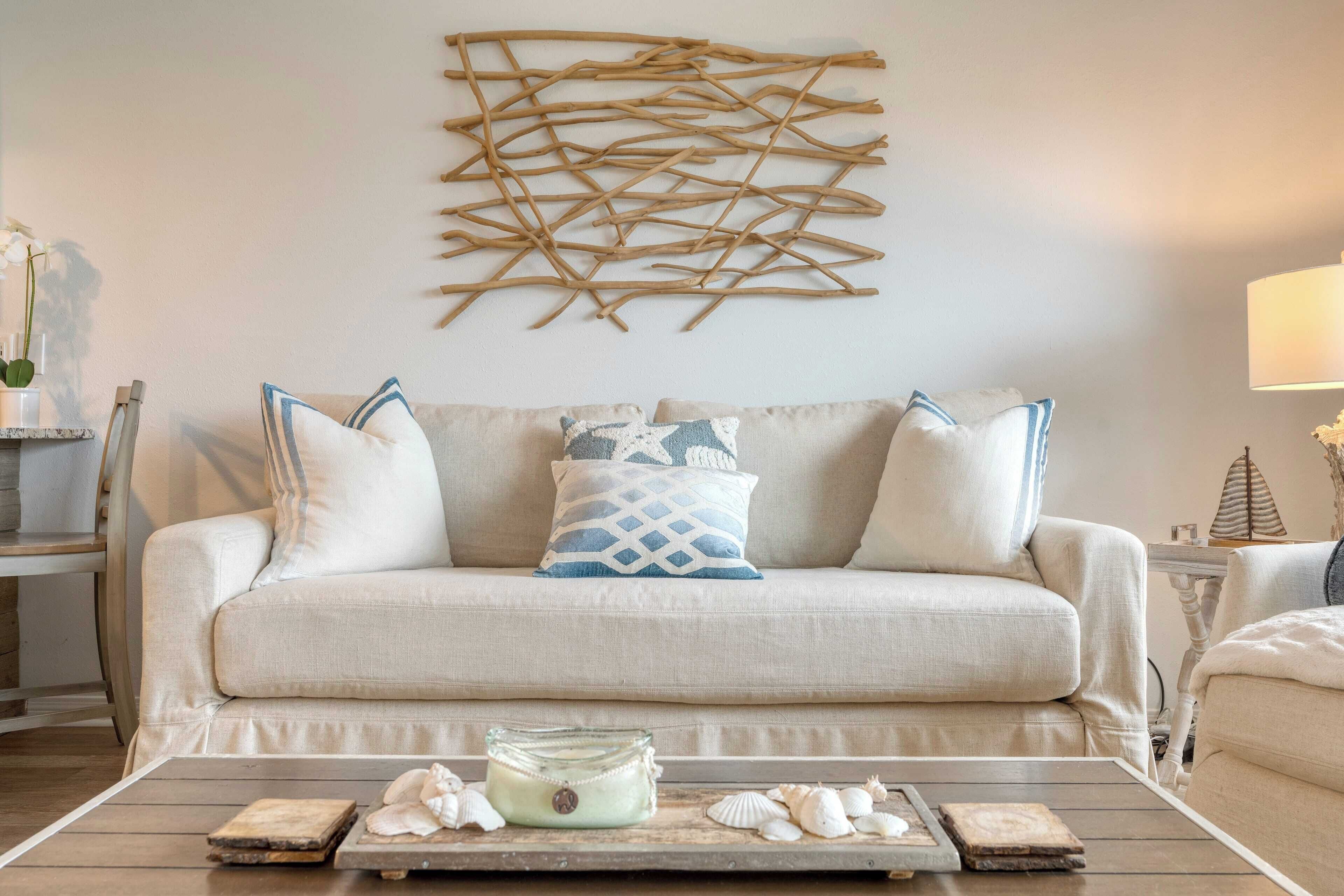 A living room with a beige sofa, decorative pillows, a wooden coffee table with seashells, and a wall art piece.