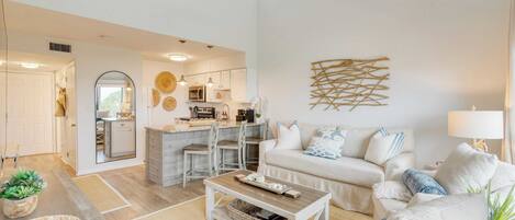 A spacious living room with a sofa, coffee table, and a kitchen area in the background.