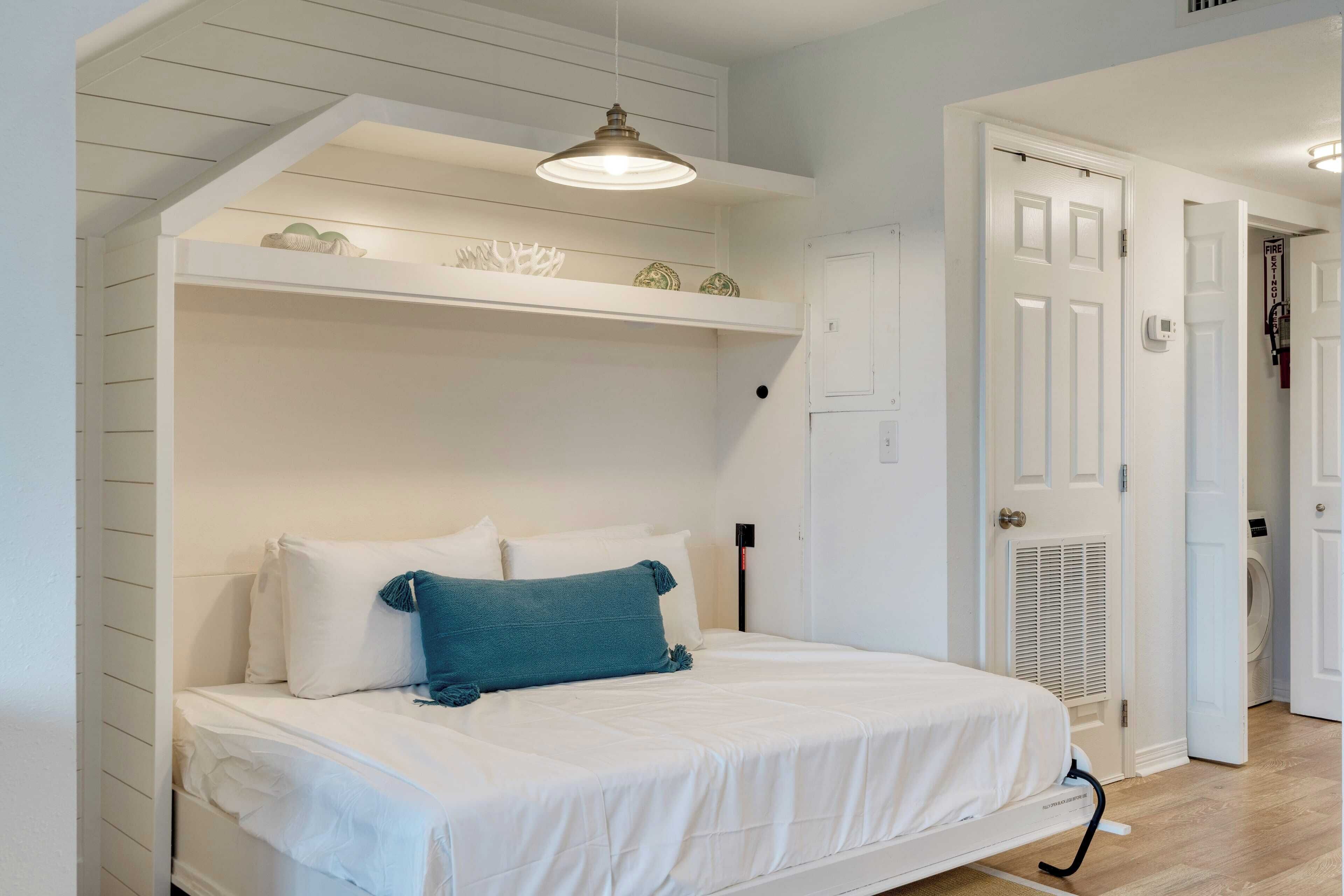 A bedroom with a bunk bed, a single bed, a pendant light, a white door, and a laundry area.