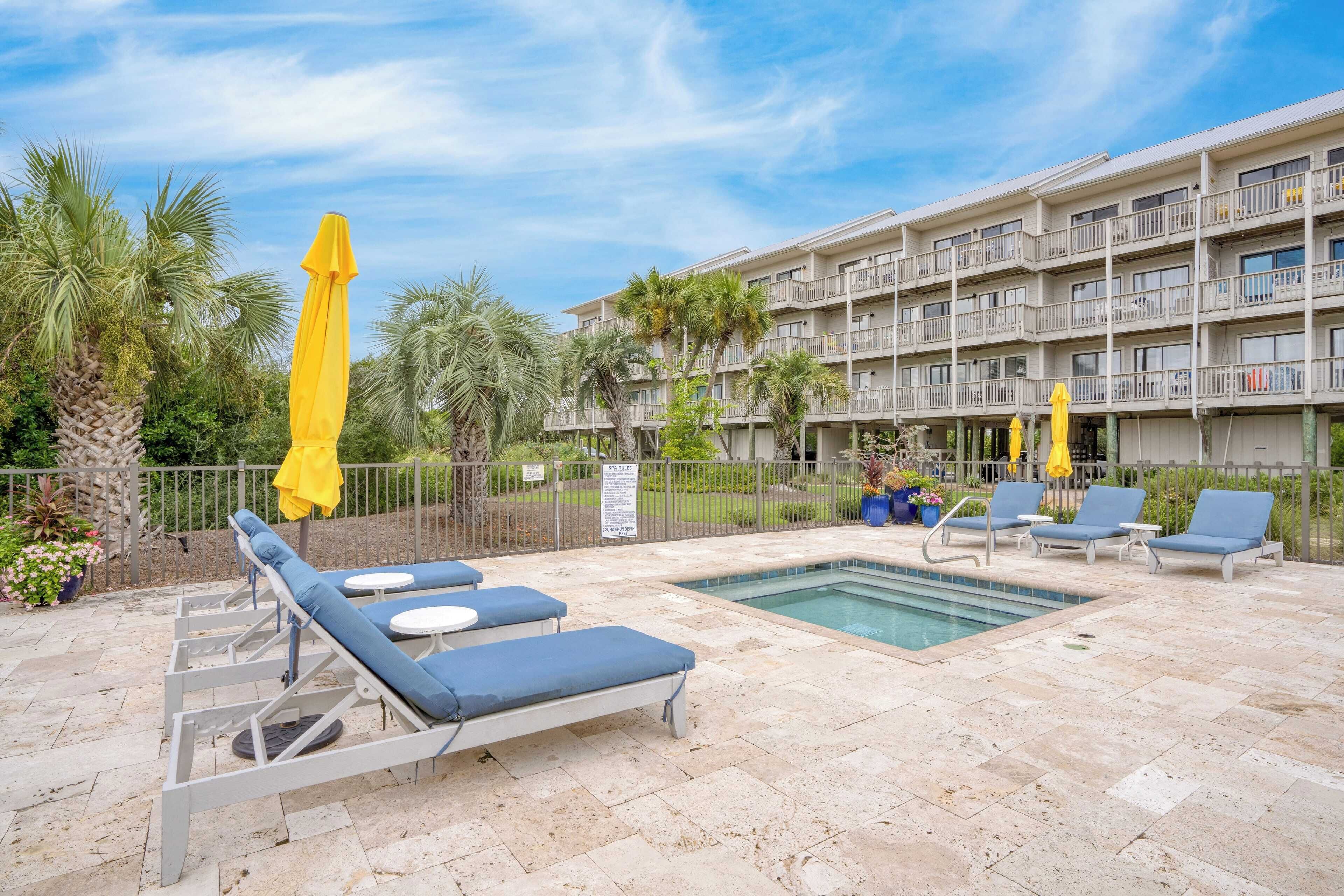 A hotel pool area with lounge chairs and umbrellas, surrounded by a fence and palm trees.