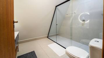Une salle de bain moderne avec une douche à parois de verre, des toilettes blanches et une porte en bois.