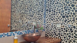 Um banheiro com toucador de madeira, pia de cobre e paredes com mosaicos.