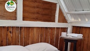 Uma cama com roupa de cama branca e manta com padrão de vaca, paredes de madeira e uma pequena mesa com toalhas.