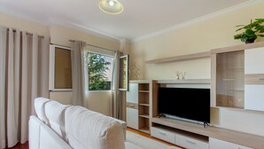 A living room with a sofa, TV, and built-in shelves. - Holiday Home 'Refugio Dourado' with Sea View, Shared Garden and Wi-Fi Access (Água de Pena)