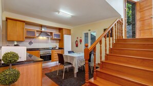 A kitchen with wooden cabinets, a dining table, and a staircase. - Holiday Home 'Refugio Dourado' with Sea View, Shared Garden and Wi-Fi Access (Água de Pena)