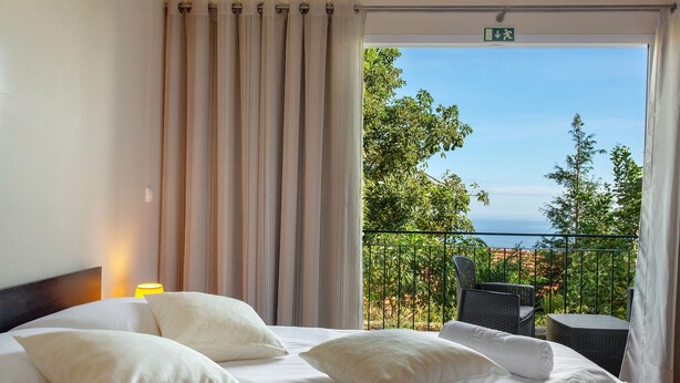 A hotel room with a bed, pillows, a neatly made bed, a balcony with a view, and a chair. - Holiday Home 'Refugio Dourado' with Sea View, Shared Garden and Wi-Fi Access (Água de Pena)