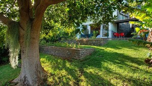 A tree-lined garden with a brick planter, a white building with a balcony, and red chairs. - Holiday Home 'Refugio Dourado' with Sea View, Shared Garden and Wi-Fi Access (Água de Pena)