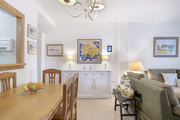 Un comedor con una mesa de madera, sillas, un armario blanco y un cuadro en la pared.