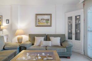 A living room with a sofa, a coffee table with seashells, a lamp, a framed picture, and a cabinet with dishes.