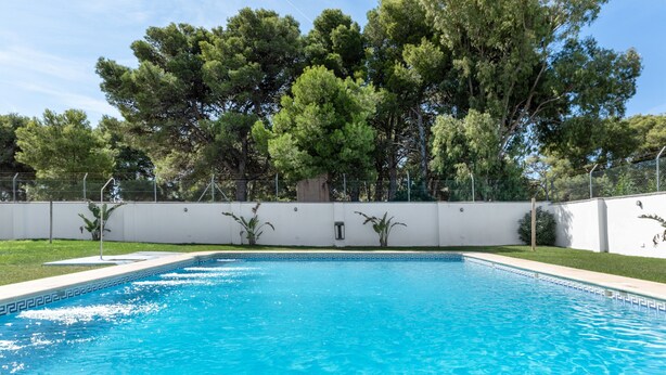 A rectangular swimming pool with clear blue water, surrounded by a white wall and a fence.