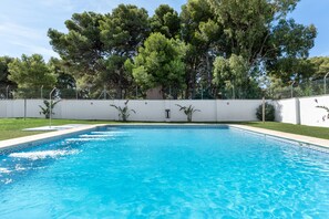 A rectangular swimming pool with clear blue water, surrounded by a white wall and a fence.