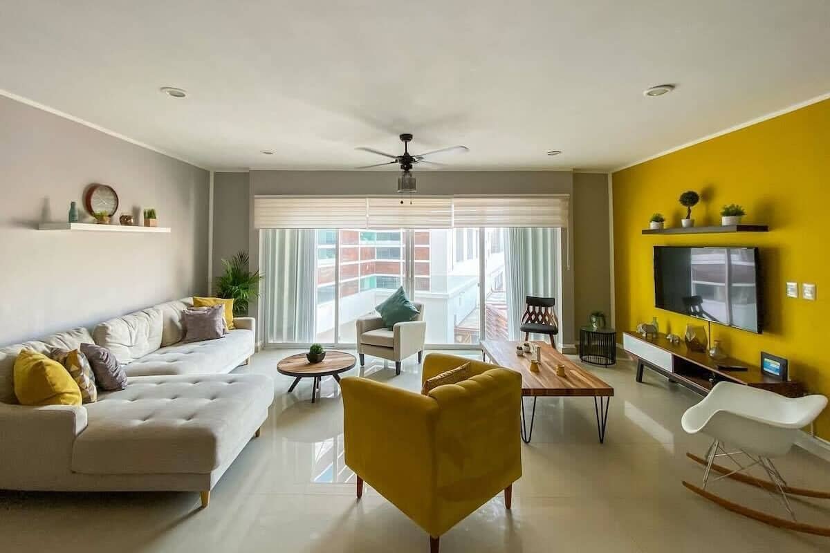 A modern living room with a sofa, yellow armchair, and a dining table.