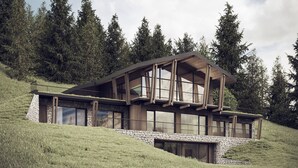 Ein modernes Haus mit Steinfundament, großen Fenstern und Holzkonstruktion auf einem grasbewachsen Hügel.