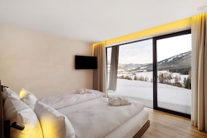 A bedroom with a large window, a flat-screen TV, and a bed with white bedding.