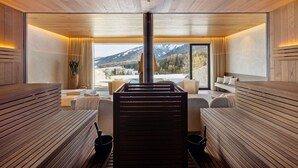 Ein Saunaraum mit Holzbänken, einer Zentralheizungsanlage und Bergblick durch große Fenster.