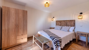 A bedroom with a wooden wardrobe, a bed with patterned pillows, a bench, and two bedside tables. - Holiday Home 'Alte Com Amor' with Mountain View, Wi-Fi and Air Conditioning (Alte)