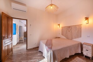 Quarto com cama, mesas de cabeceira, luminária pendente e ar-condicionado fixado na parede.