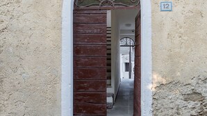 A narrow entrance with a wooden door and a metal gate, leading into a building with a white exterior and a number '12' sign.