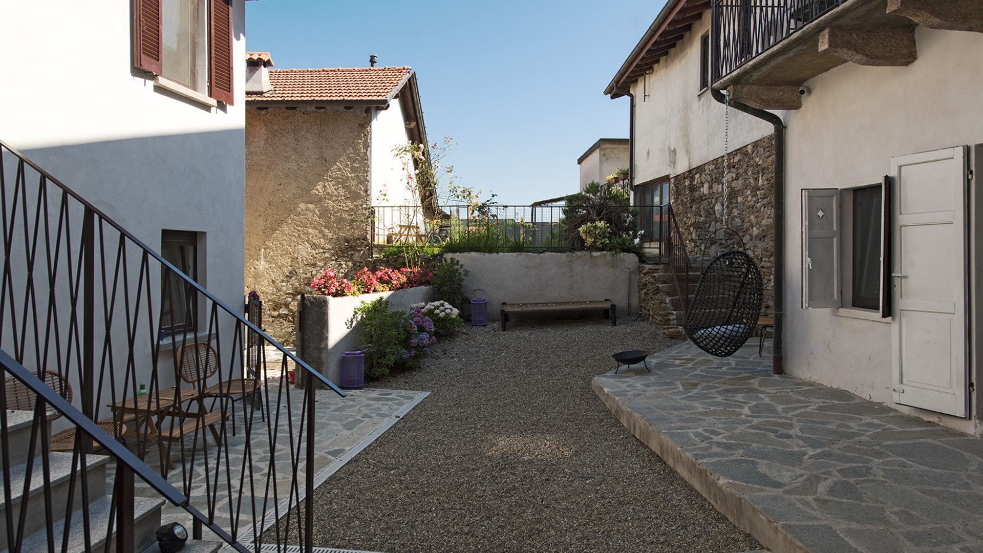 A narrow courtyard with a stone pathway, a bench, and a hanging chair.
