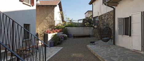 A narrow courtyard with a stone pathway, a bench, and a hanging chair.