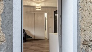 A hallway with a wooden floor, a black chair, a white door, and a hanging light fixture.