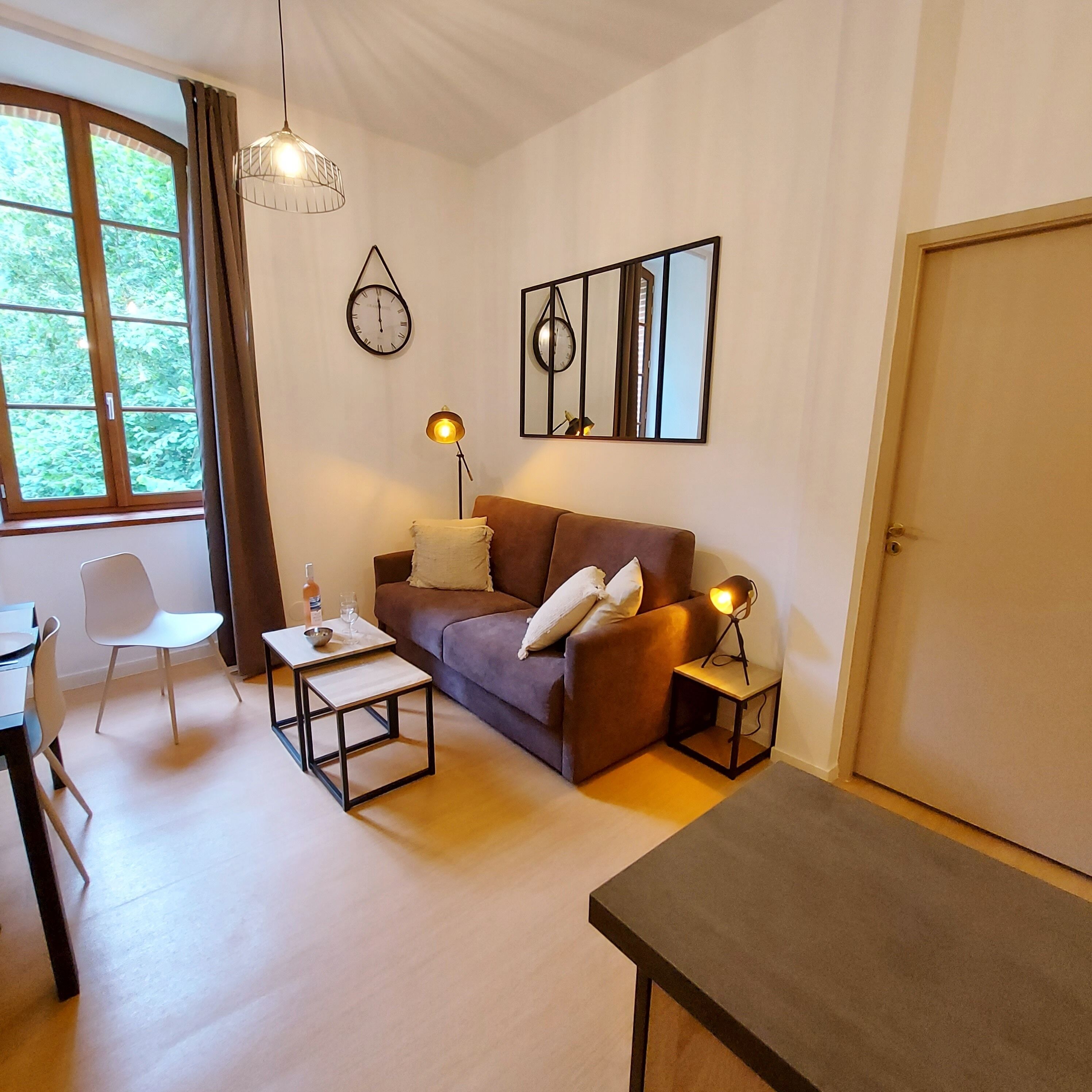 A modern living room with a brown sofa, a white chair, a small table, and two floor lamps.