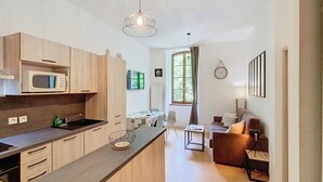 A modern kitchen with wooden cabinets, a microwave, and a dining area with a table and chairs. - Magnificent 3 stars flat (Aulus-les-Bains)