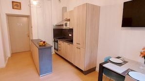 A modern kitchen with wooden cabinets, a built-in microwave, and a small island. There is a dining area with a table and chairs, and a flat-screen TV mounted on the wall. - Magnificent 3 stars flat (Aulus-les-Bains)