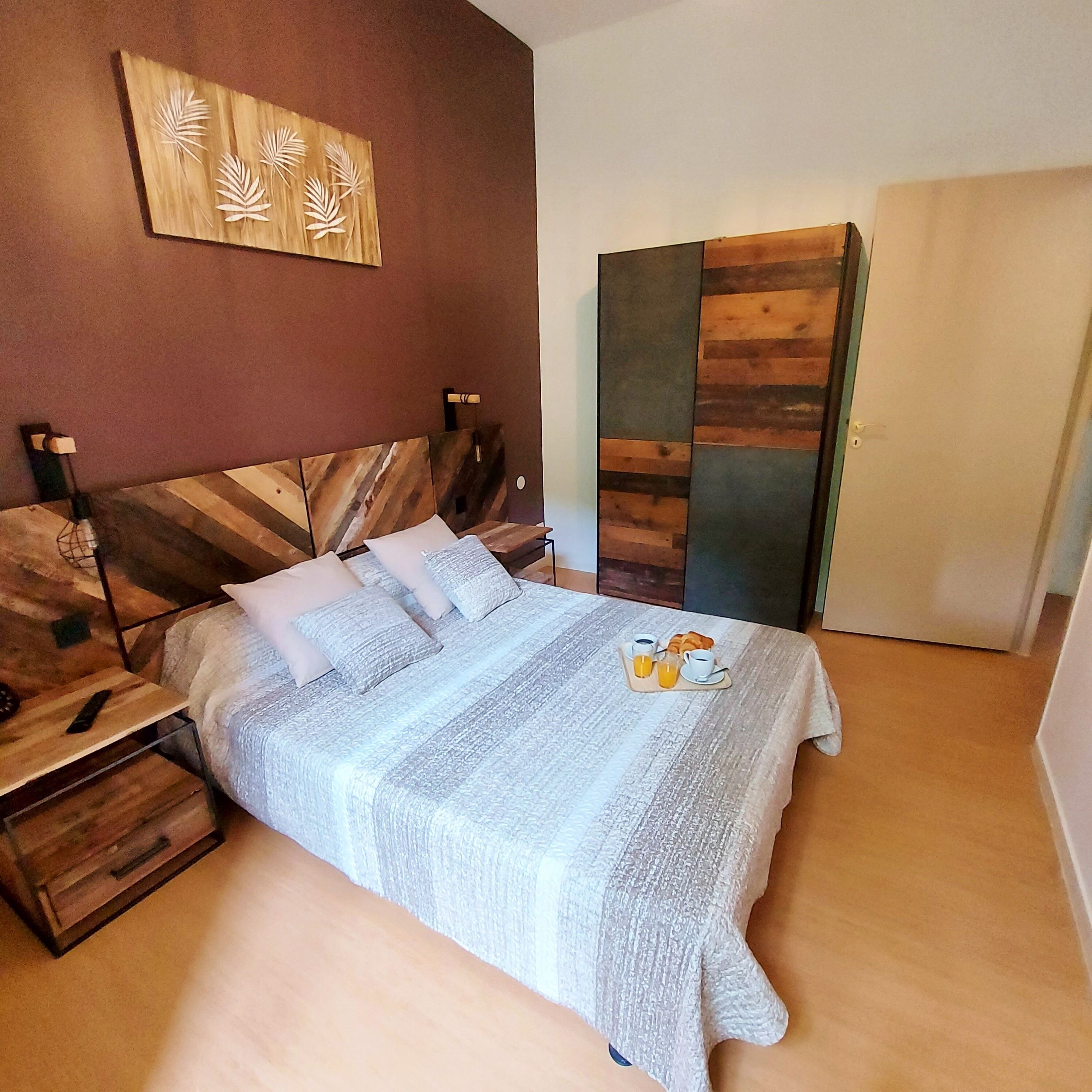 Un lit bien fait, recouvert d’une couverture à rayures, une table de chevet avec une lampe, et une œuvre d’art accrochée au mur au-dessus.